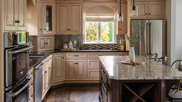 A modern kitchen with light wood cabinets, a large island, stainless steel appliances, and a window providing natural light.