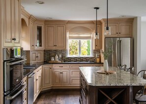 Une cuisine moderne avec des meubles en bois clair, un grand îlot central, des appareils électroménagers en acier inoxydable et une fenêtre qui laisse entrer la lumière naturelle.
