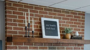 A brick fireplace with a shelf above it holding a sign that reads "stay humble, work hard."