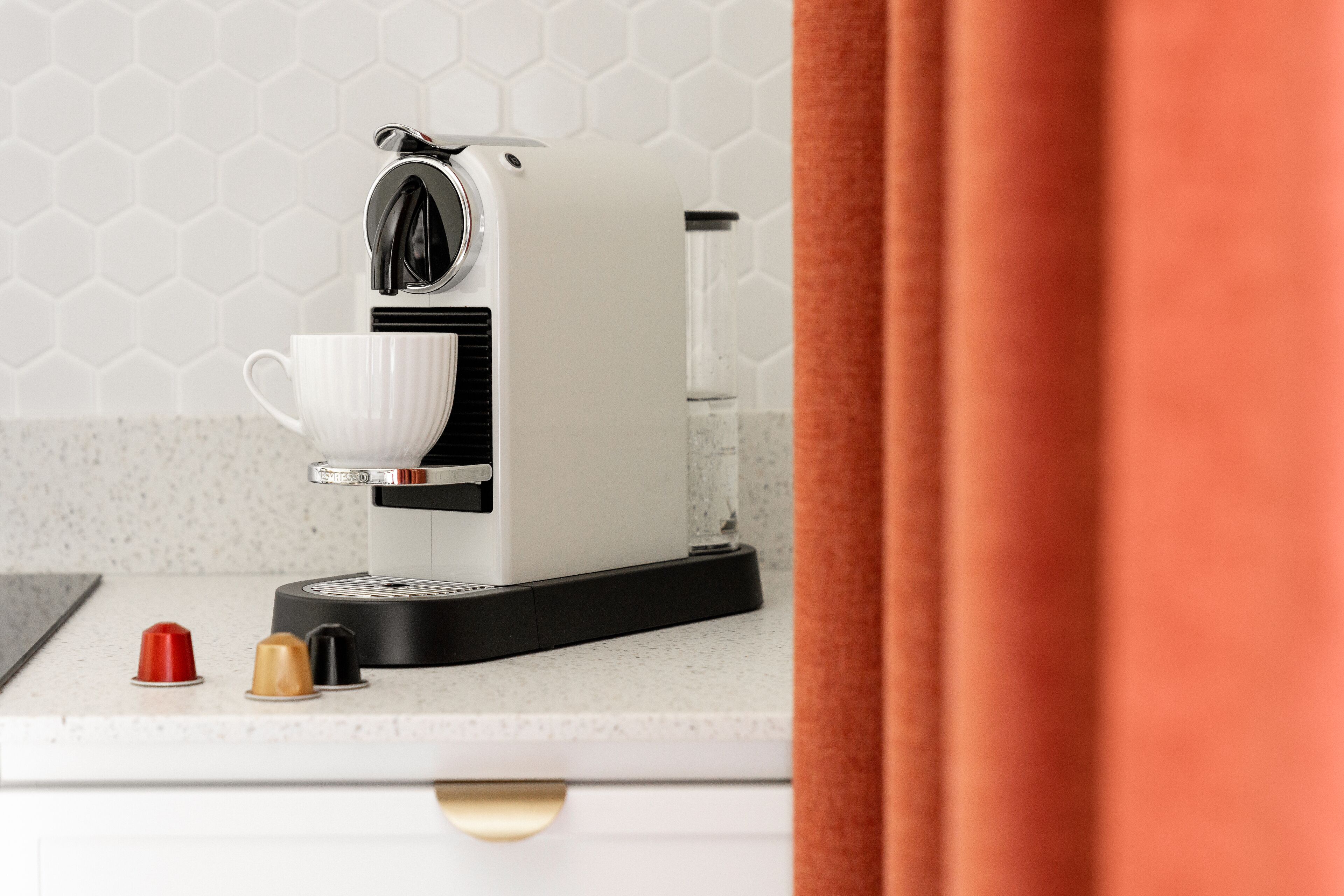Una moderna macchina per il caffè su un piano di lavoro in cucina, con un portabicchieri bianco e un erogatore d'acqua.
