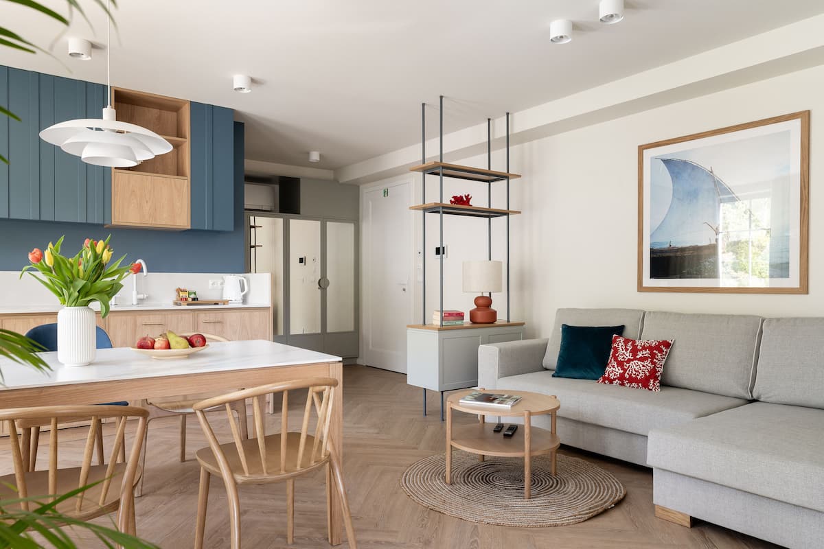 A modern living room with a sofa, a dining table with chairs, a coffee table, and a kitchen area with cabinets and a hanging light fixture.