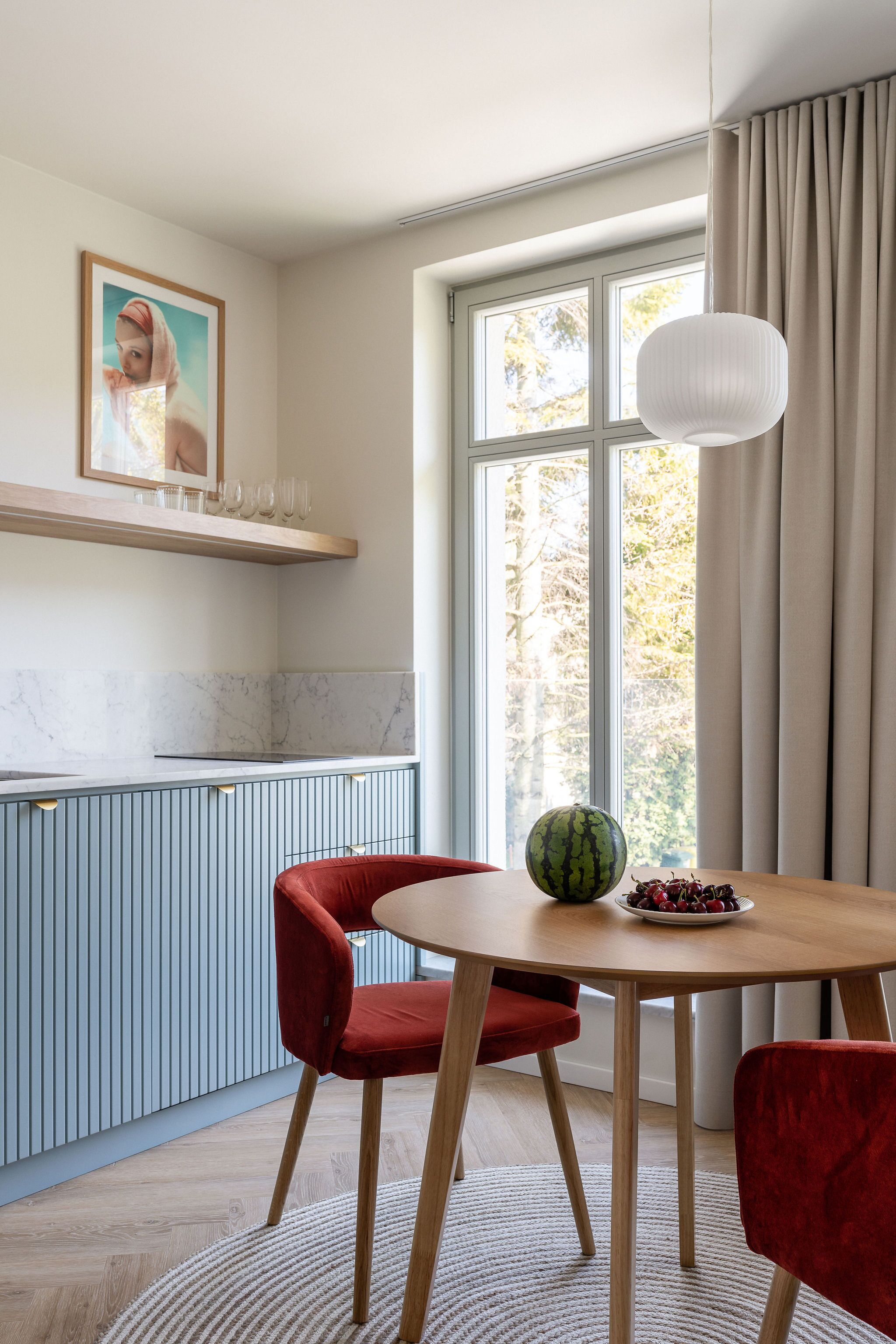 A modern kitchen with a marble countertop, a red chair, a wooden table, and a hanging light fixture.