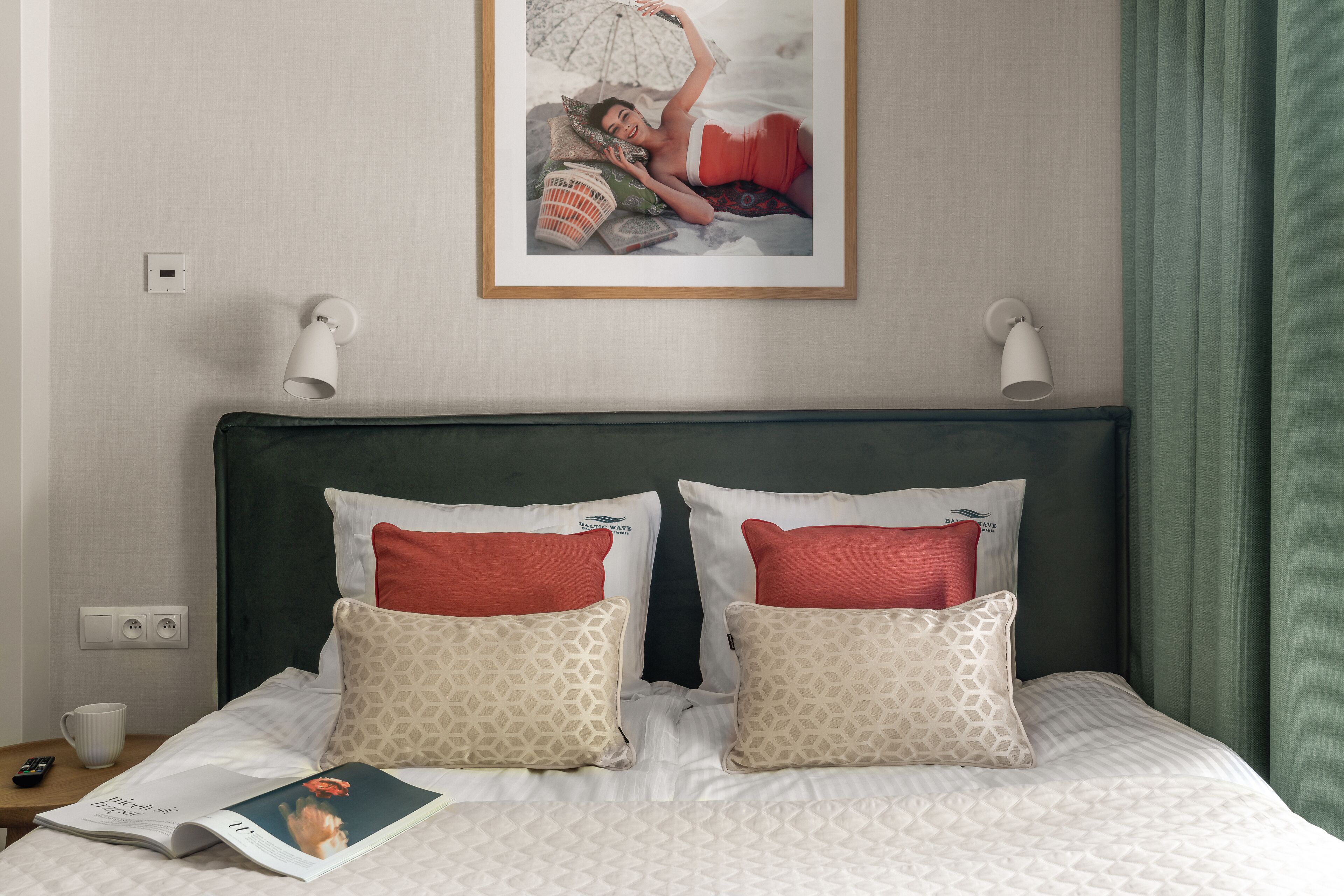 A neatly made bed with patterned pillows, a framed photo on the wall, and a magazine on the nightstand.