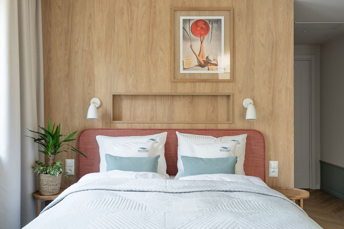 A neatly made bed with white and teal pillows, a framed picture on the wall, and a potted plant on a bedside table.