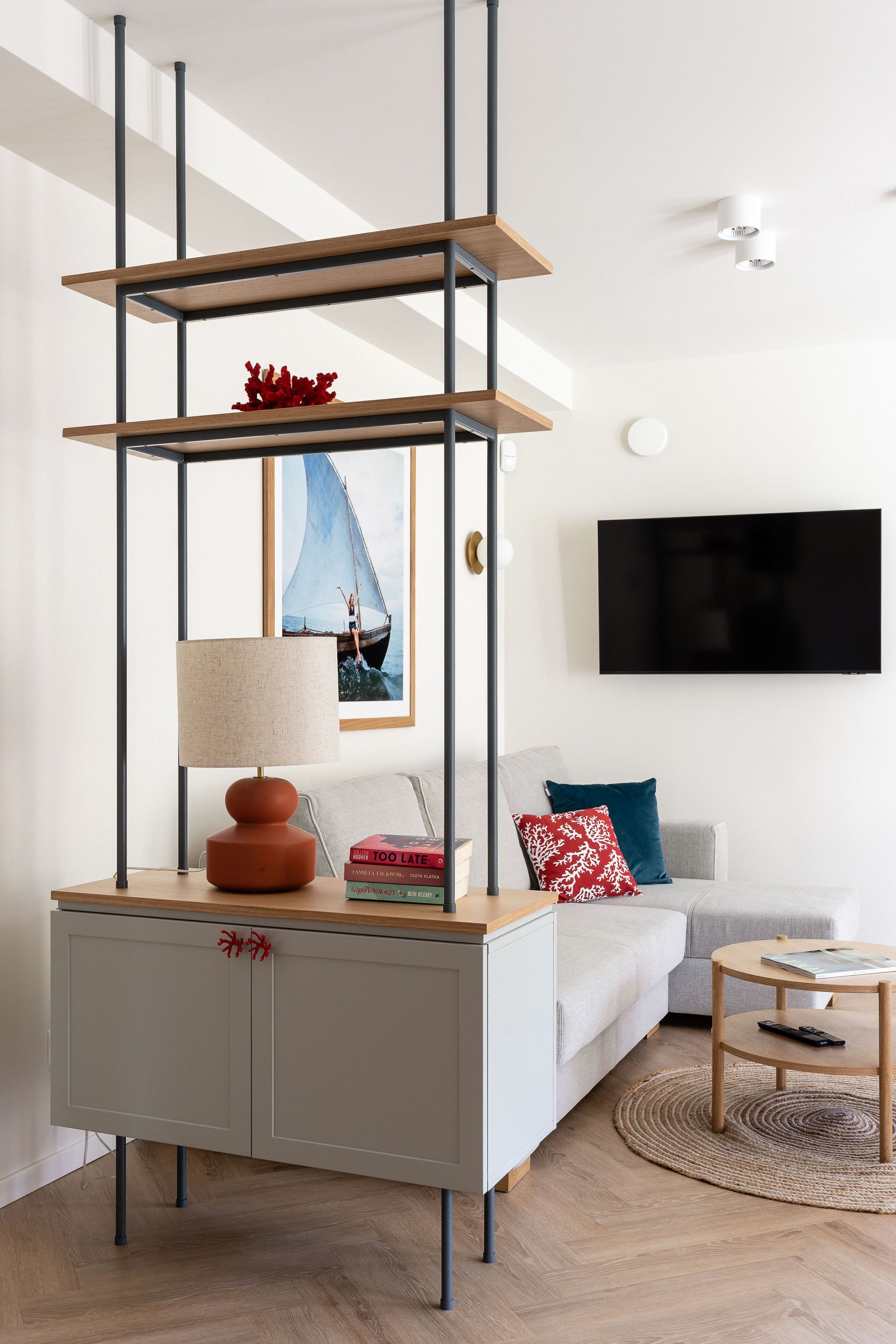 A modern living room with a grey sofa, a wooden coffee table, a TV mounted on the wall, and a unique shelving unit with a lamp.