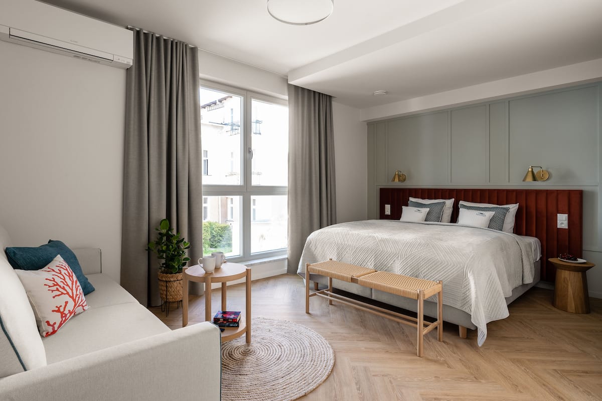 A modern bedroom with a large bed, a sofa, a small table, and a bench.