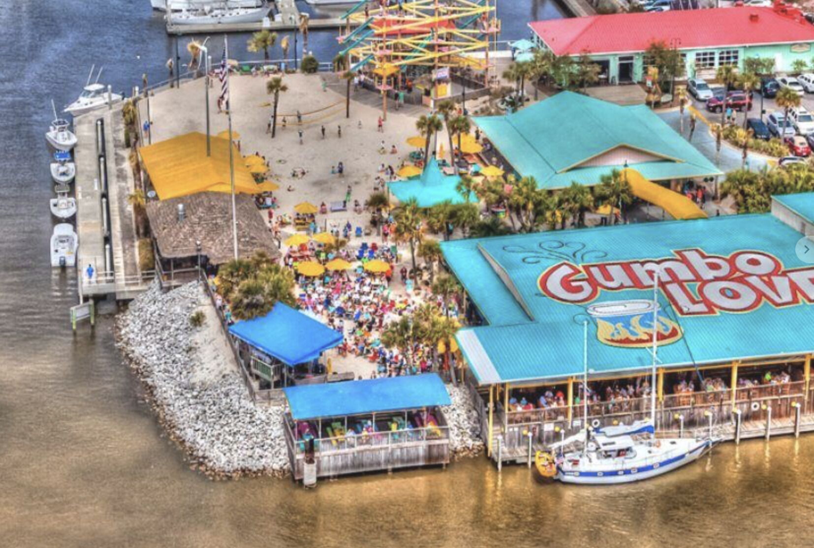 Une zone côtière comprenant un grand parc d’attractions, un quai pour bateaux et un bâtiment sur lequel on peut lire l’inscription « Gumbo Lovin’ ».