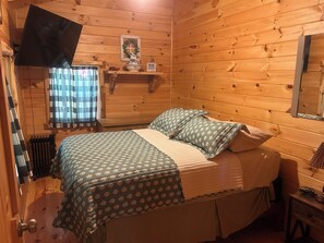 A wooden-paneled room with a bed, a window with curtains, a shelf with decorative items, and a mirror. - Luxury Amish-Built Log Cabin, Private Beach, Zip Line, ATV & Golf Cart Rentals (Ray)