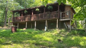 A wooden cabin with a balcony, surrounded by dense forest.