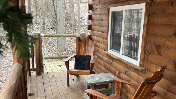 A wooden cabin with a porch featuring two rocking chairs and a small table.