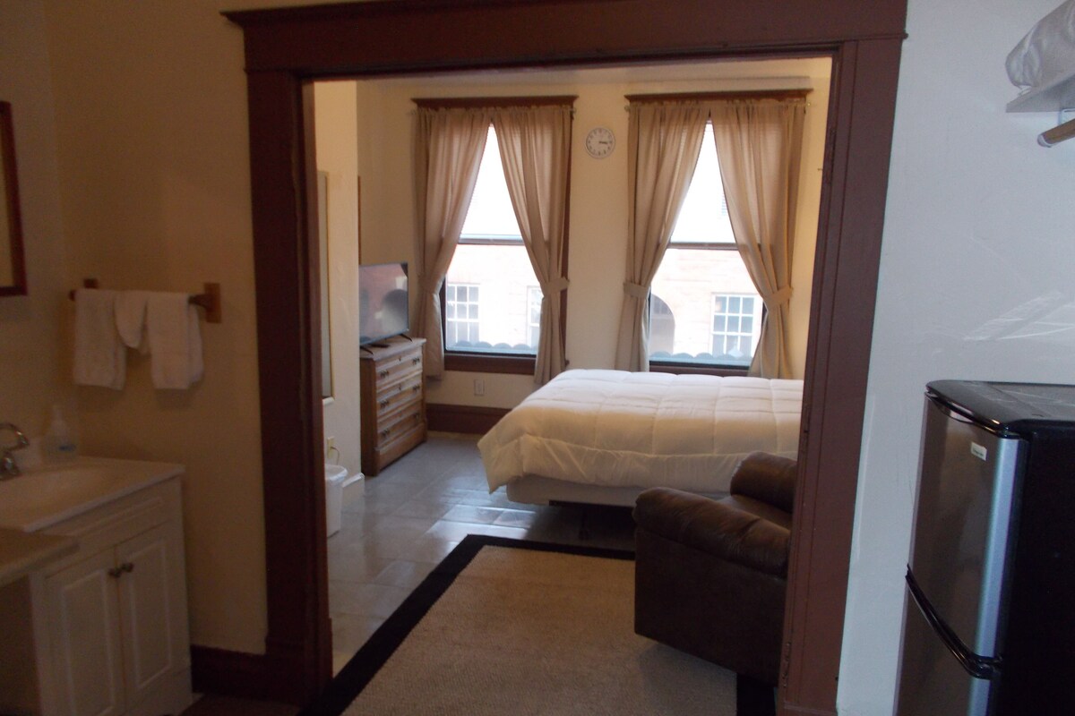 A bedroom with a bed, a dresser, a television, and a bathroom with a sink and towel rack.