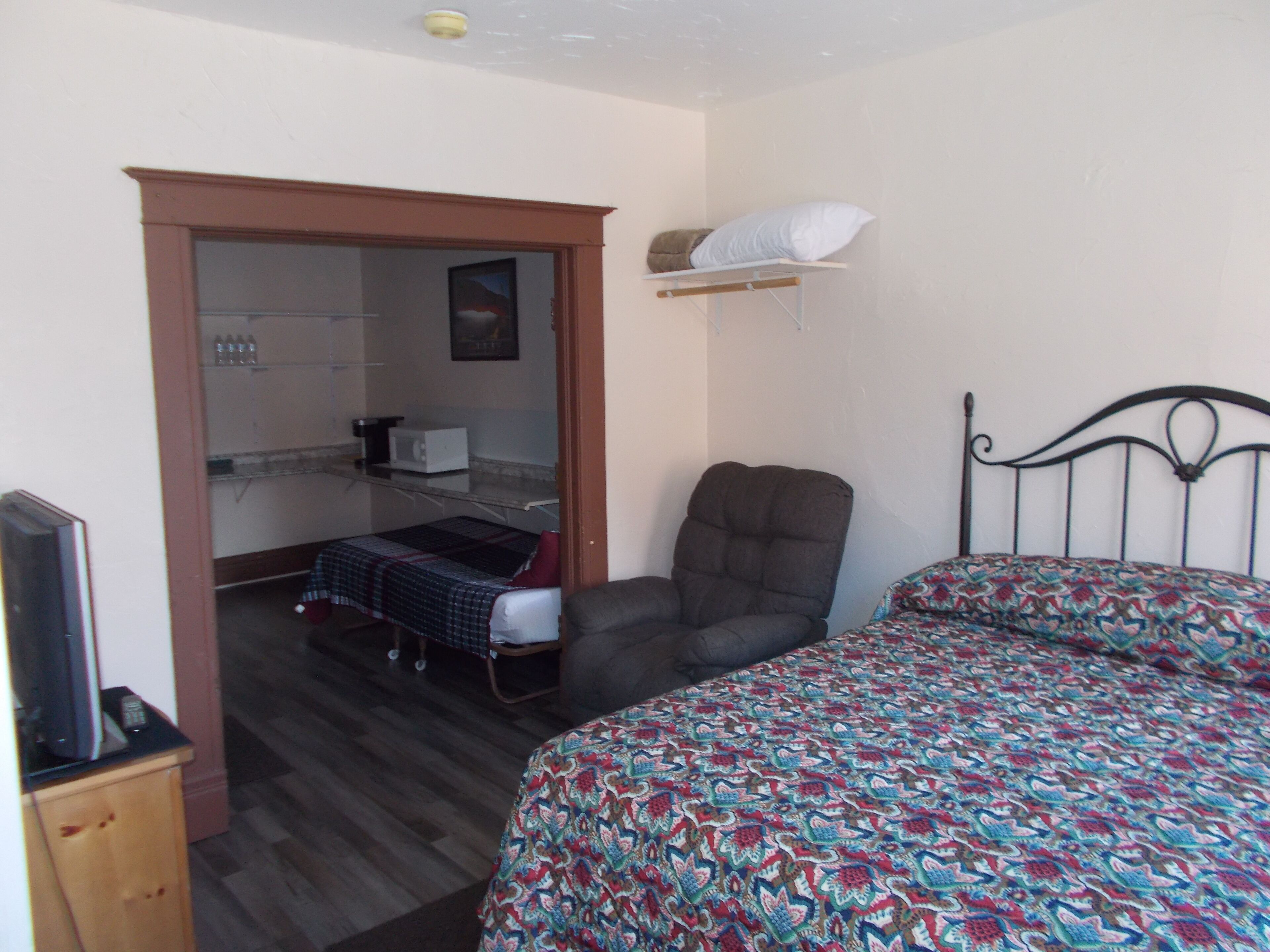 A bedroom with a bed, a chair, a small table, and a kitchenette area.