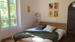A bedroom with a wooden bed, white bedding, and a window with a view of trees. There are four botanical prints on the wall. - Grande Maison Traditionnelle Proche de la Forêt (Brunoy)