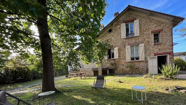 A stone building with a stone roof, a small garden with grass, a tree, and outdoor furniture including a table and chairs. - Grande Maison Traditionnelle Proche de la Forêt (Brunoy)