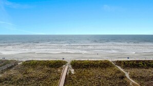 Une plage avec une promenade en bois qui mène au rivage, entourée de dunes herbeuses.