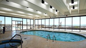 Une piscine intérieure avec de grandes baies vitrées, un poste de surveillance pour les sauveteurs et un panneau indiquant la zone peu profonde.