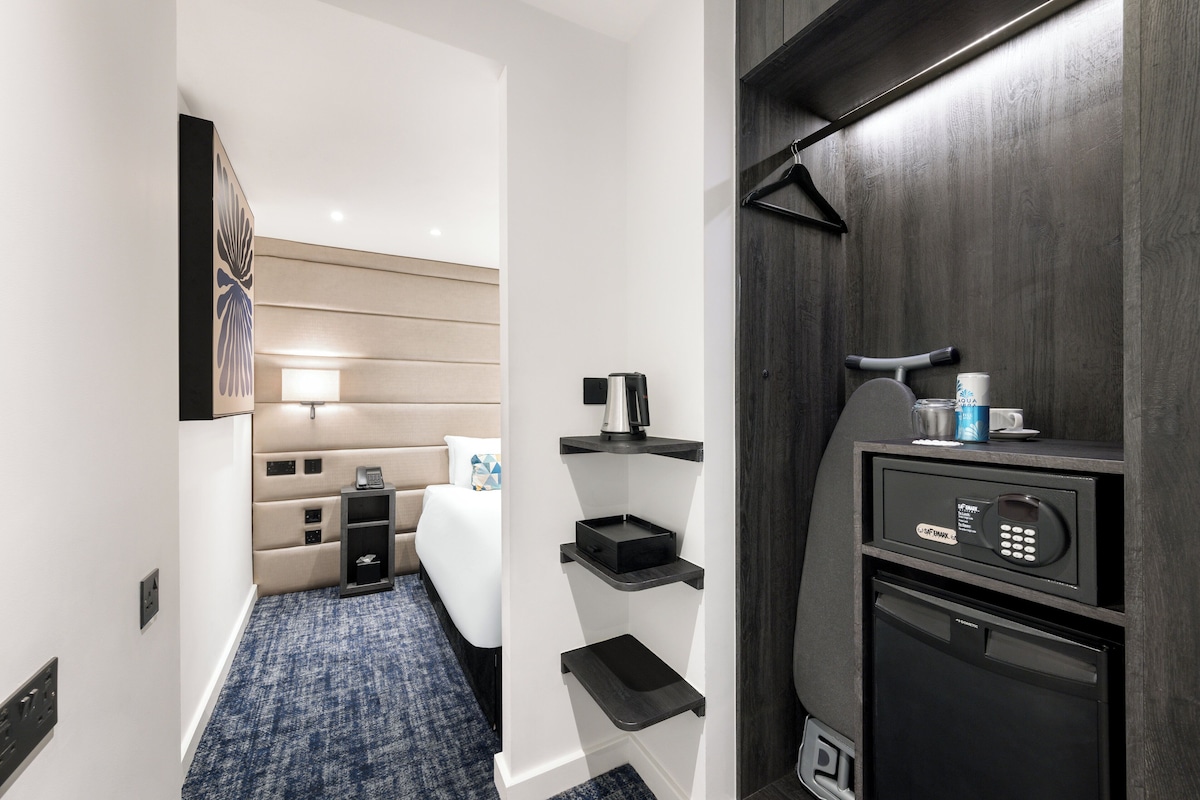 A hotel room with a bed, bedside table, and a minibar.