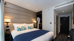 A hotel room with a large bed, bedside lamps, a robe, and a door leading to another room. - voco London Marylebone by IHG (London)