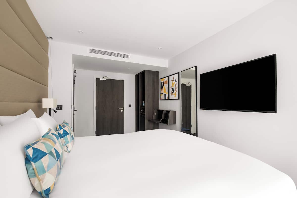 A modern hotel room with a large bed, a flat-screen TV, a wardrobe, and a door leading to a bathroom.