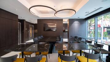 A modern dining area with multiple tables and chairs, a large window offering a view of the city, and a contemporary ceiling design.