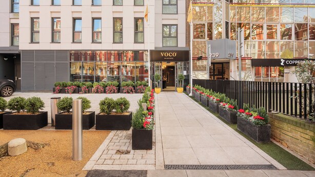 A hotel entrance with a modern facade, a visible entrance, and a well-maintained garden area with potted plants and flowers. - voco London Marylebone by IHG (London)