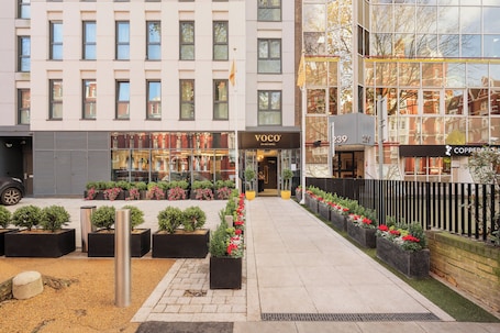 A hotel entrance with a modern facade, a visible entrance, and a well-maintained garden area with potted plants and flowers.