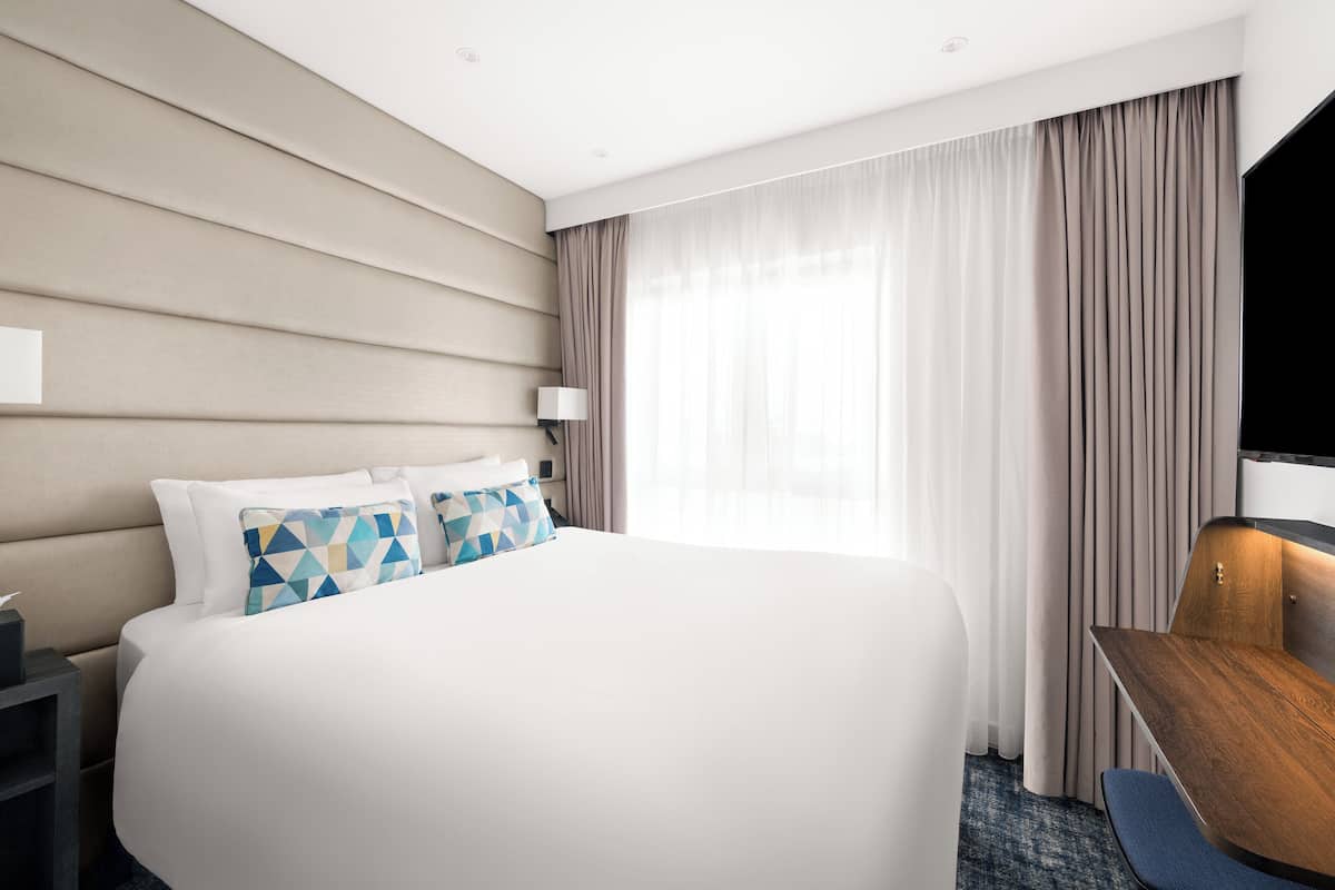 A modern hotel room with a large bed, a desk, and a TV.