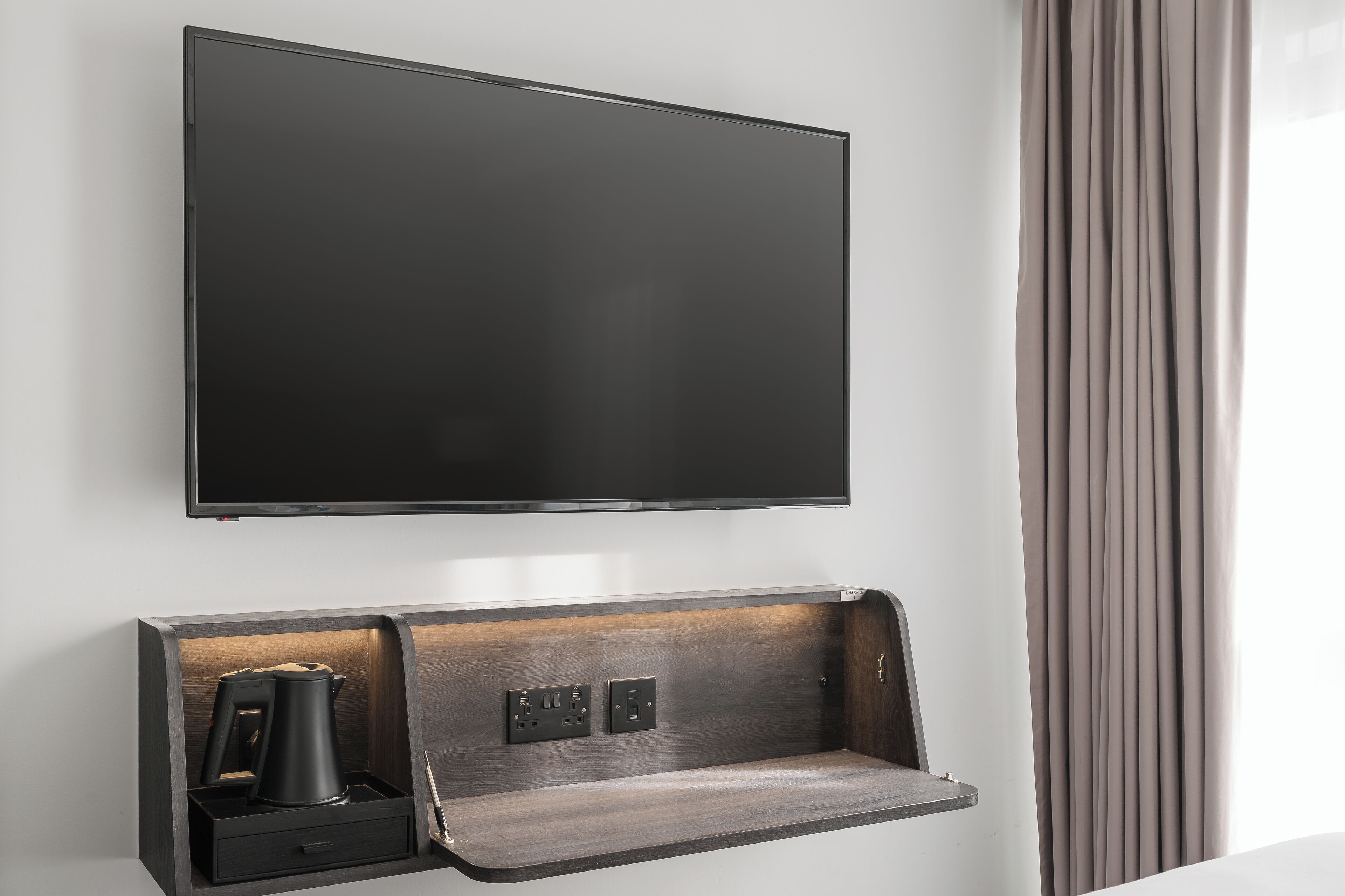 Ein moderner, an der Wand befestigter Fernseher mit integriertem Ablagebereich darunter.