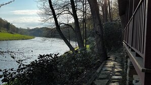 Un sentier de pierres bordant une rivière, avec des arbres et un bâtiment sur la droite.