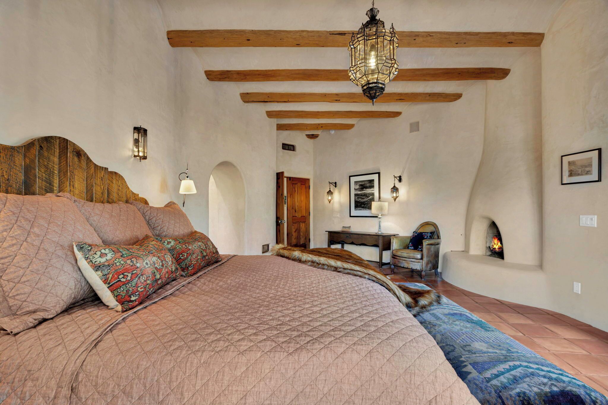 Un dormitorio espacioso con una cama grande, vigas de madera, chimenea y un candelabro.