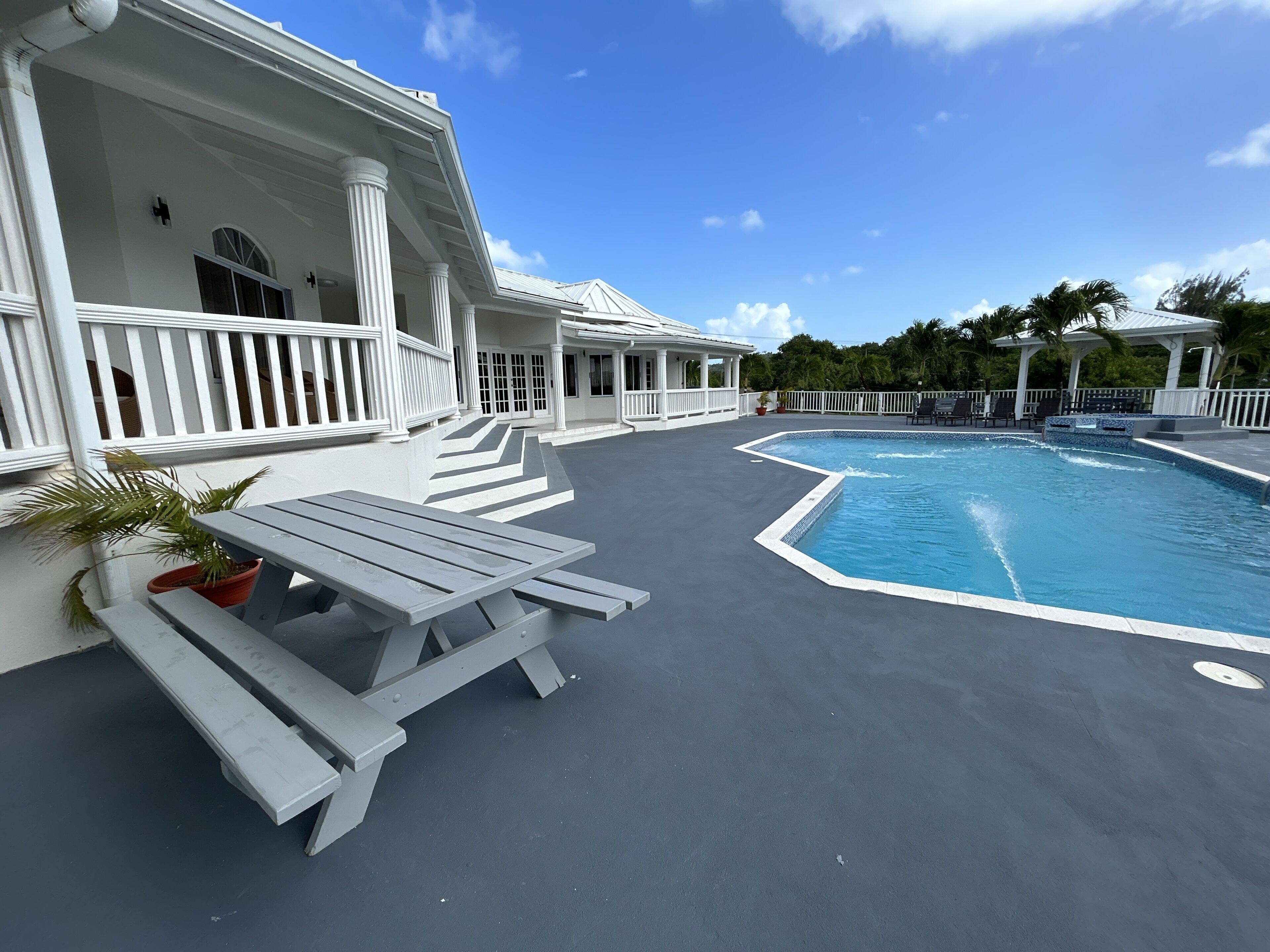 A pool area with a covered patio, white columns, and a seating area with a table and chairs.