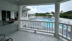 A covered outdoor area with a pool, white columns, and a view of a lush landscape.