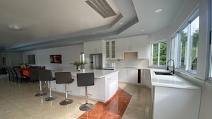 A modern kitchen with white cabinets, a central island with bar stools, and a large window providing natural light.