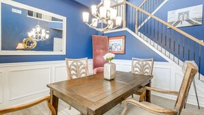 Ein Essbereich mit Holztisch und Stühlen, einer Chandelierleuchtre und einer Treppe mit Geländer.