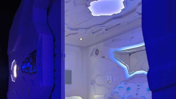 Una habitación futurista con una cama, paneles de control y una pared con interfaz digital.