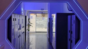 Un pasillo con taquillas, un letrero que dice 'SALIDA' y una lámpara de diseño geométrico en la pared.