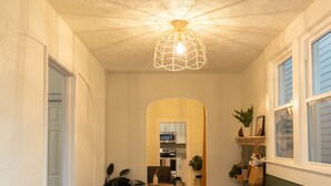 Un couloir avec un plancher en bois, un luminaire au plafond, un banc et des plantes en pot.