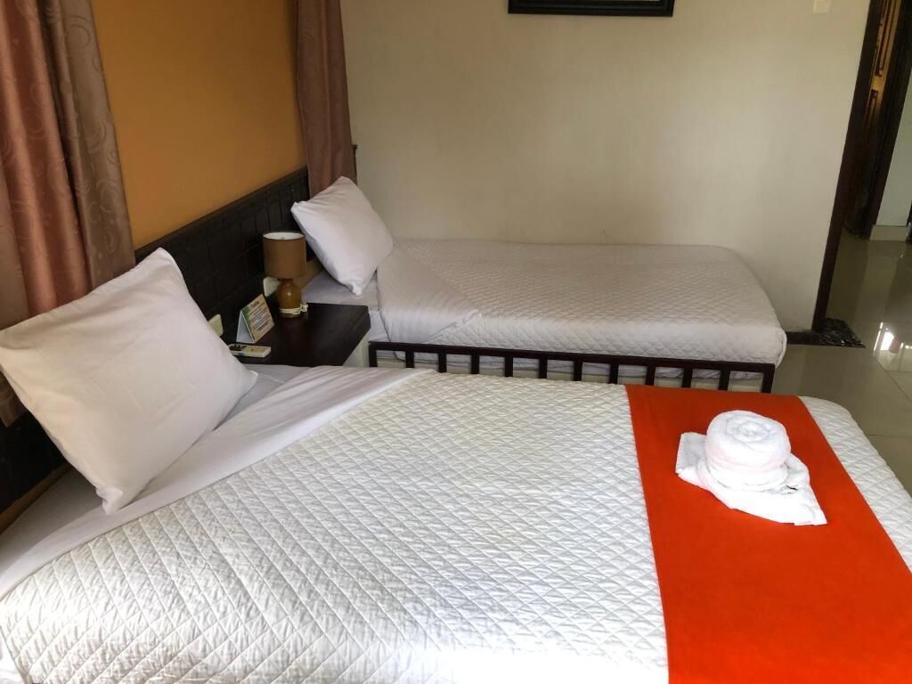 A hotel room with two beds, a nightstand with a lamp, and a red towel on the bed.