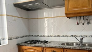 A kitchen with white tiled walls, a granite countertop, wooden cabinets, a stainless steel sink, and a gas stove. - Nazaré Corner House -1 mim from the beach (Nazaré)