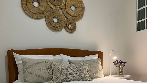 A neatly made bed with a white comforter and multiple pillows, a wooden headboard, and a wall-mounted decorative item above the bed. - Nazaré Corner House -1 mim from the beach (Nazaré)
