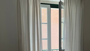 A room with a bed, a chair, and a door leading to an outdoor area with a balcony. - Nazaré Corner House -1 mim from the beach (Nazaré)