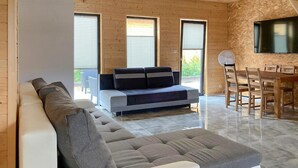A modern living room with a sofa, a dining table with chairs, and large windows. - Pet friendly home in Jantar with sauna (Jantar)