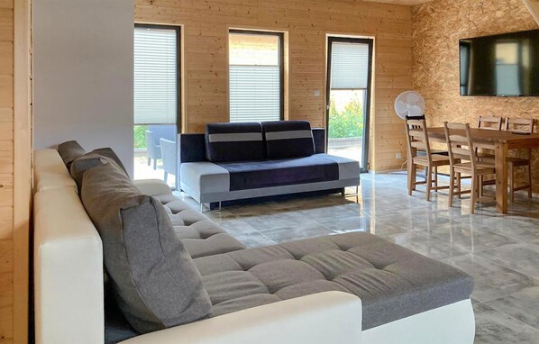 A modern living room with a sofa, a dining table with chairs, and large windows.