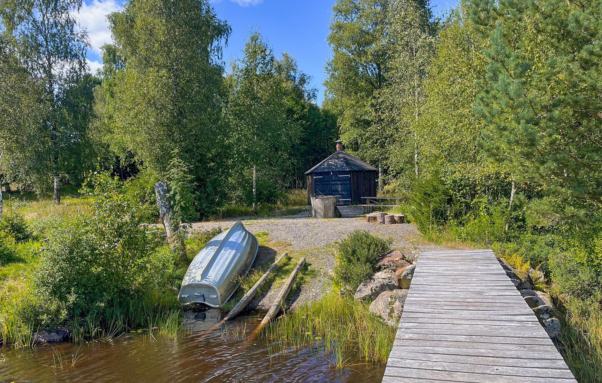 A wooden dock leading to a small wooden structure with a chimney, surrounded by dense forest.