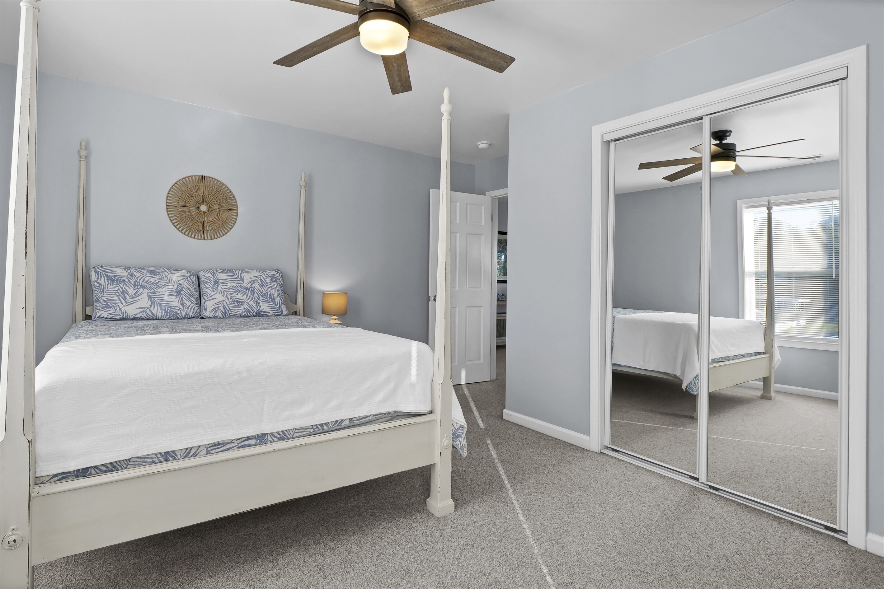 Une chambre à coucher avec un lit à baldaquin blanc, un ventilateur de plafond, un objet décoratif fixé au mur et un grand miroir.