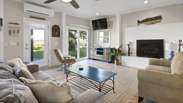A spacious living room with a ceiling fan, a fireplace, and a large window overlooking a garden. - A Turtle's View-Waterfront-Dock-Fenced Yard-Dog Friendly (Surf City)