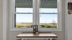A room with a wooden table and two stools, a window with a view of a field and a bridge, and a sign on the wall. - A Turtle's View-Waterfront-Dock-Fenced Yard-Dog Friendly (Surf City)