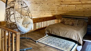 Un dormitorio acogedor con una hamaca colgante, una cama con colcha estampada y techo de madera.