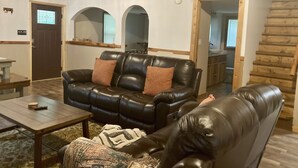 Una sala de estar acogedora con un sofá de cuero negro, una mesa de centro de madera y un plaid estampado.