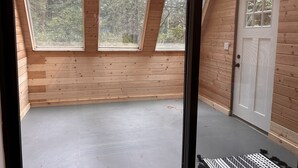 A room with wooden walls and a sloped ceiling with skylights, a grey floor, and a white door. - Bandon Country Club (Bandon)